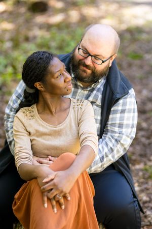 Couple sitting together outdoors wearing casual clothing embracing in a tender moment amidst nature. Ottawa Wedding Photographer