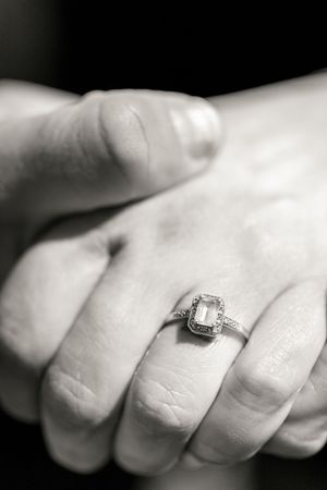A black and white close-up photograph shows an elegant diamond engagement ring on a hand with clasped fingers. Ottawa Wedding Photographer
