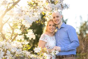 A couple poses together outdoors among beautiful blooming white magnolia flowers on a sunny spring day. Ottawa Wedding Photographer