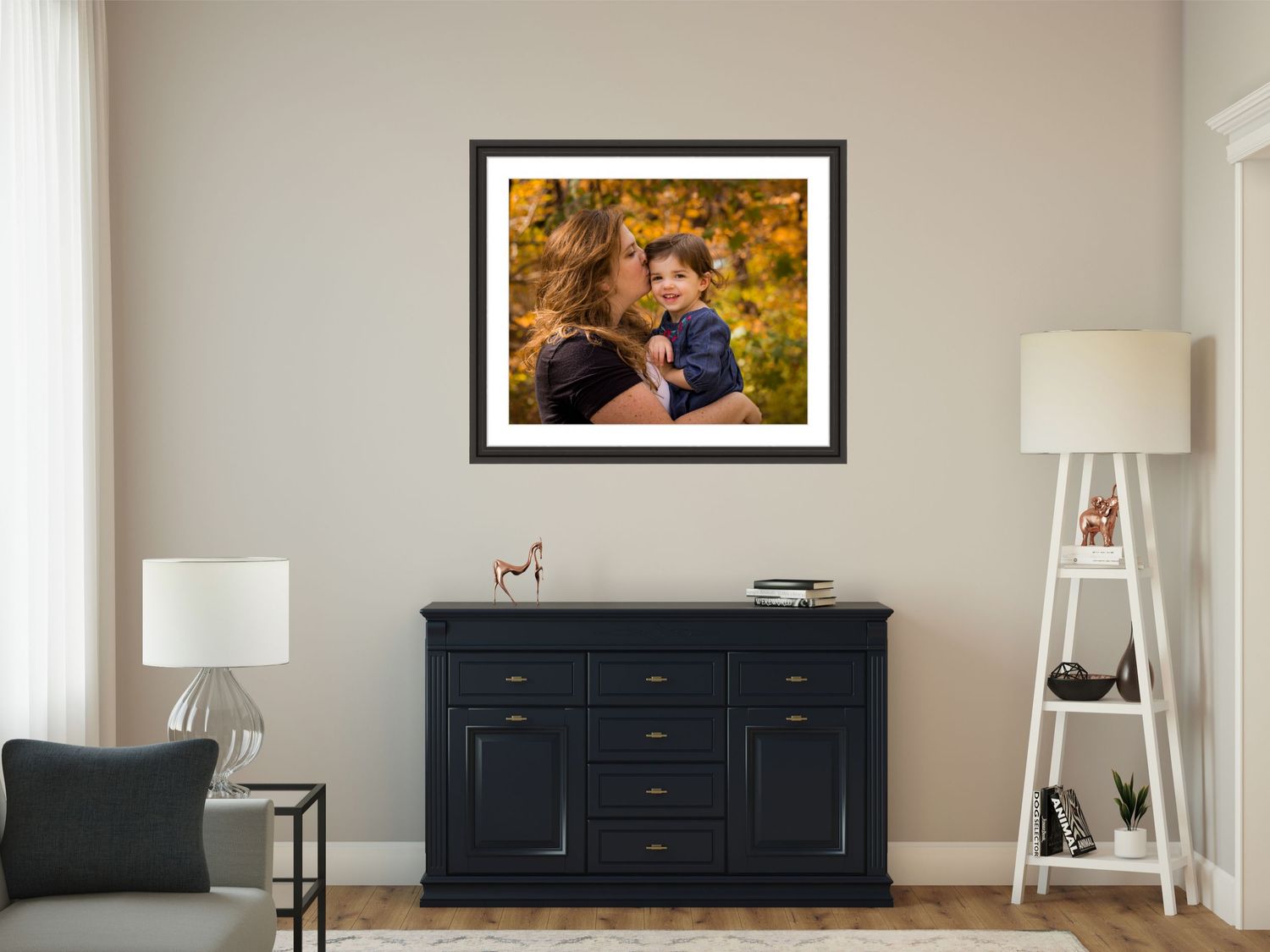 A framed photograph displayed above a dark blue dresser in a modern living room with white walls and decorative elements.