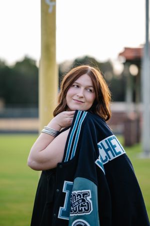 A casual portrait with a letterman jacket in an outdoor sports field setting.