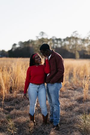 A couple in casual attire sharing an intimate moment while standing in a golden sunlit field at sunset.