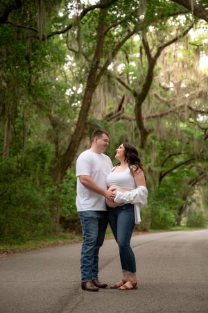 A loving couple shares a romantic moment on a tree-lined path covered in Spanish moss.