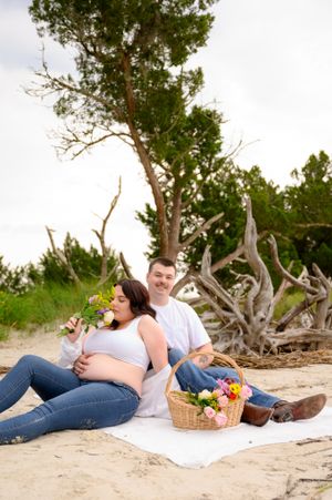 A loving couple relaxes on a beach blanket with a picnic basket and colorful flowers.