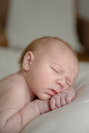 A peaceful sleeping newborn baby rests on soft white bedding.