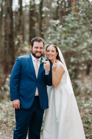 Beautiful outdoor wedding photo of a couple in classic blue suit and white dress smiling together in a forest setting.