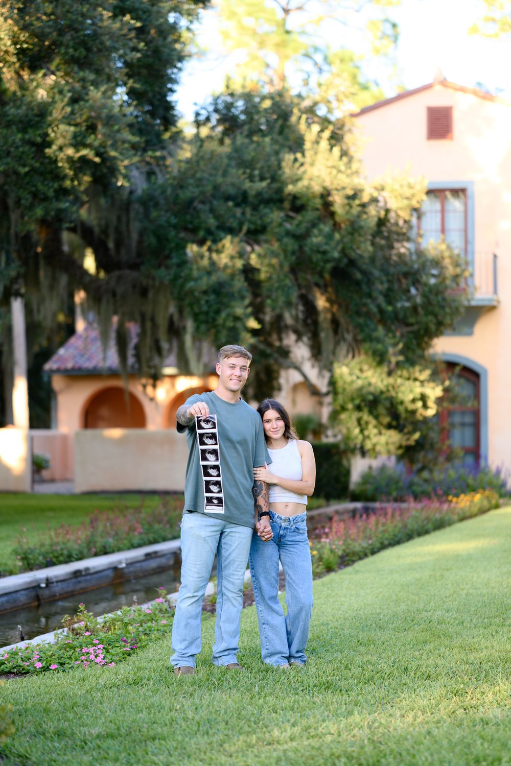 Couple standing on manicured lawn in front of Mediterranean-style building.