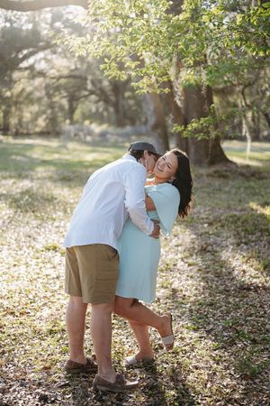 Couple embraces in a romantic moment under sunlit trees in a dreamy outdoor park setting.