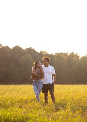 Couple walking together in a sunlit meadow during golden hour.