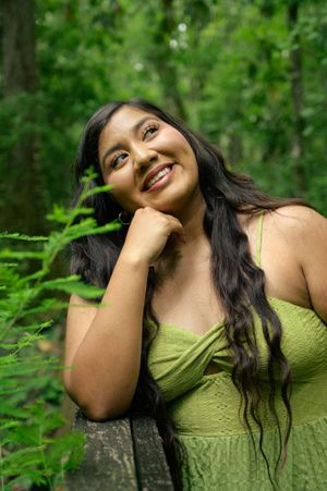 Portrait of woman in green dress smiling against lush forest background.