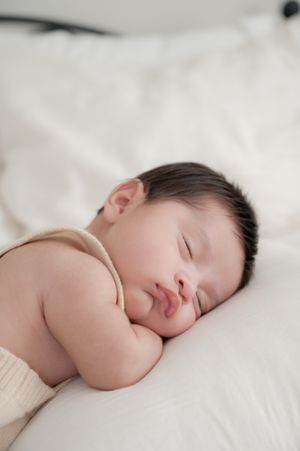 Sleeping infant in neutral tones peacefully resting on white bedding.