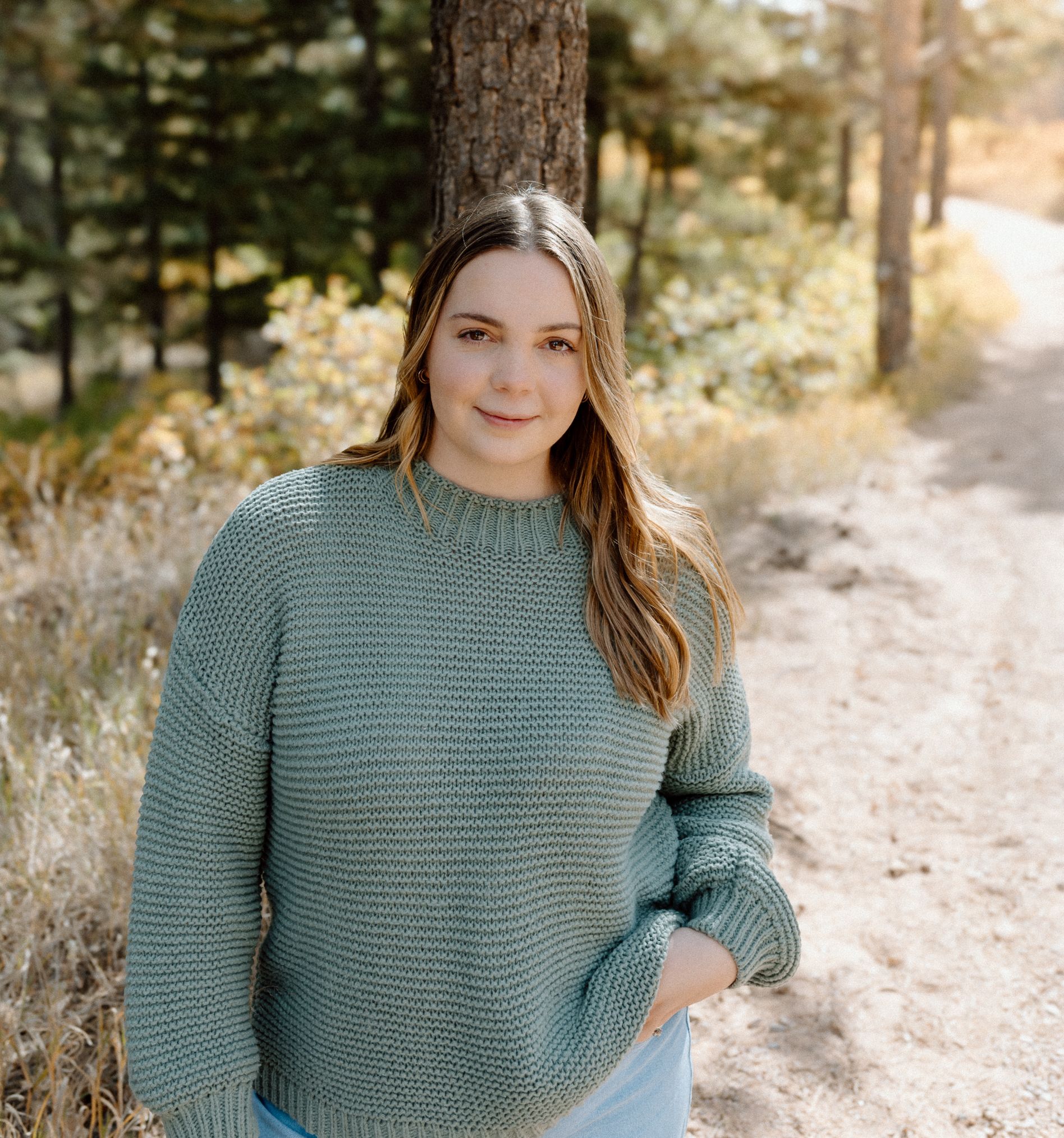 Someone wearing a sage green knit sweater standing on a forest path. Colorado Springs Photographer.