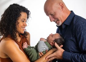 A tender family moment shared between parents and their infant baby against a white background.