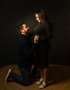An intimate maternity photo of an expectant couple in dark clothing against a black background.