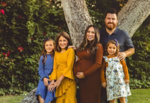 A family of five poses together against a tree with colorful outfits in an outdoor setting.