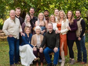 Large extended family poses together for a group photo outdoors with fall foliage in background.