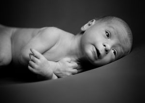 A black and white portrait of a newborn baby lying on their side.