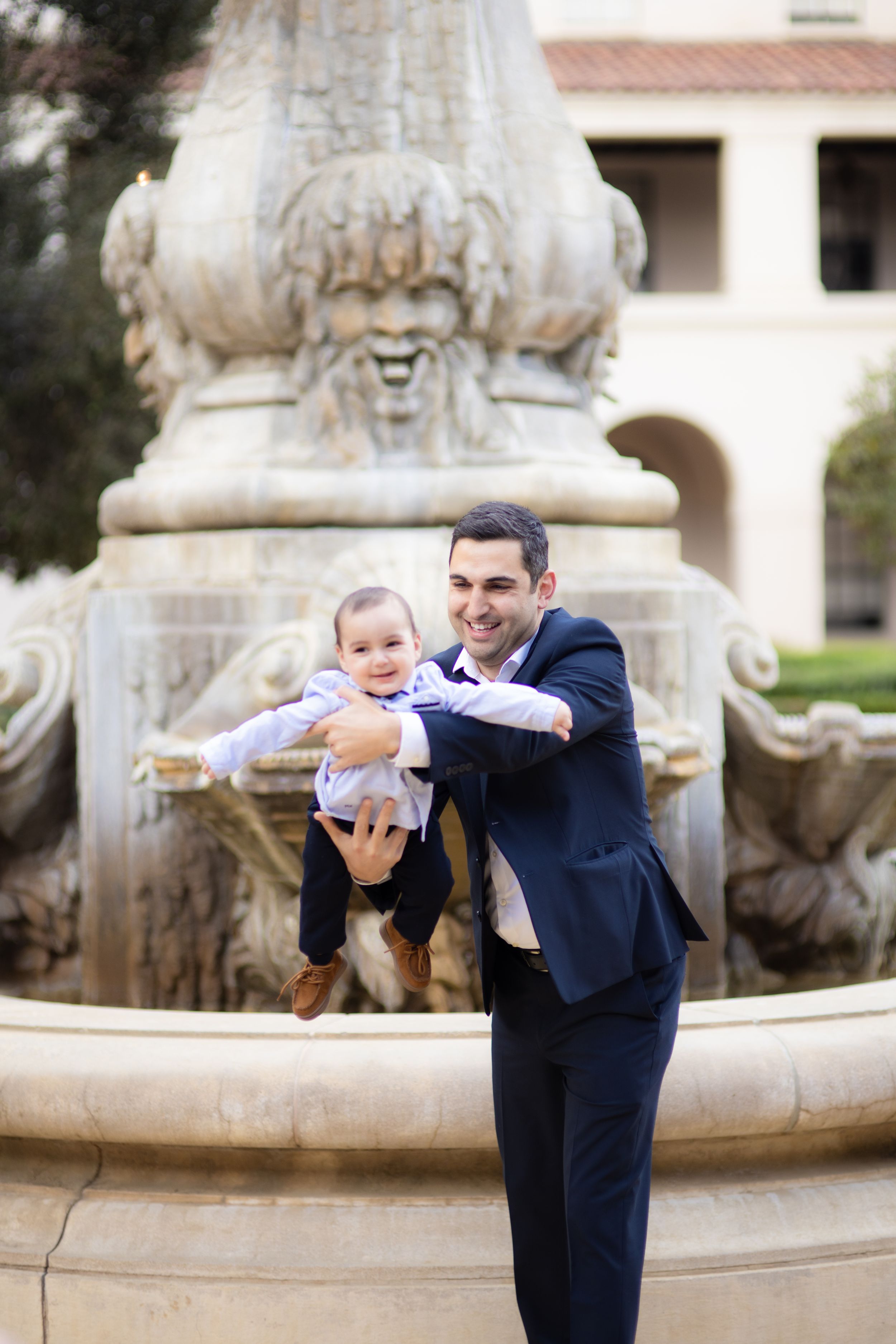 Playful father and child pose together by an ornate stone fountain.
