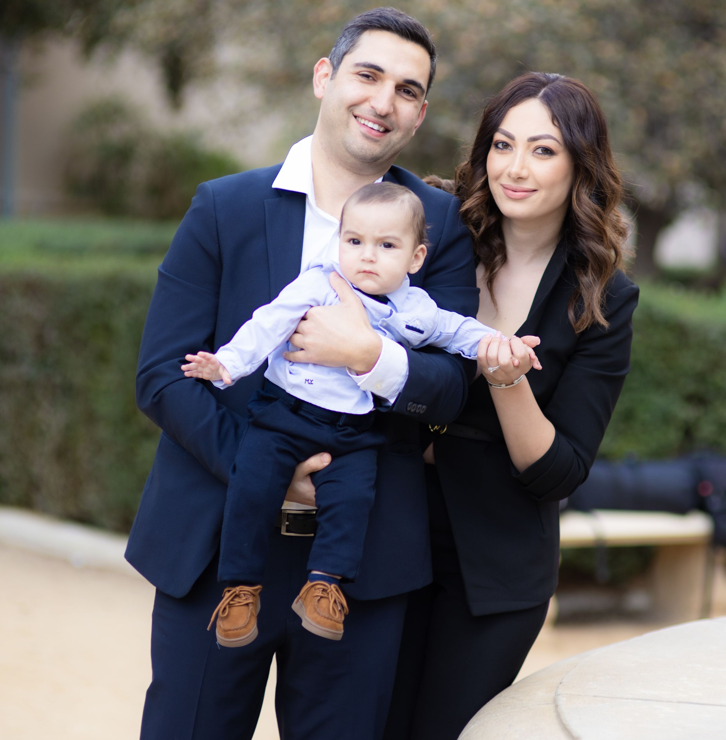 Elegant family portrait with baby wearing formal attire outdoors.