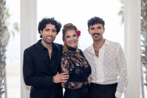 Three people in formal attire posing together under white columns.