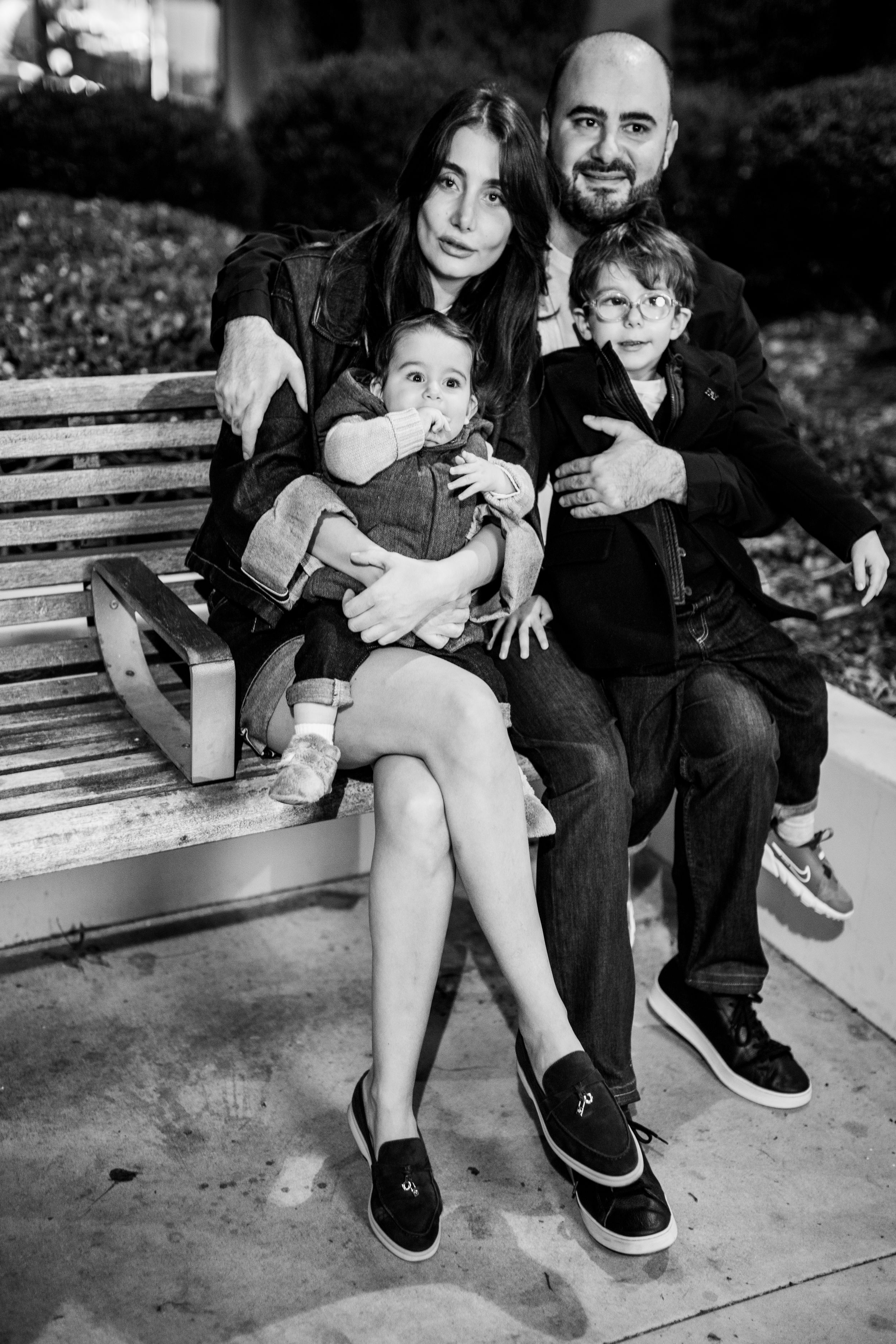 Family sitting together on wooden bench in black and white portrait.