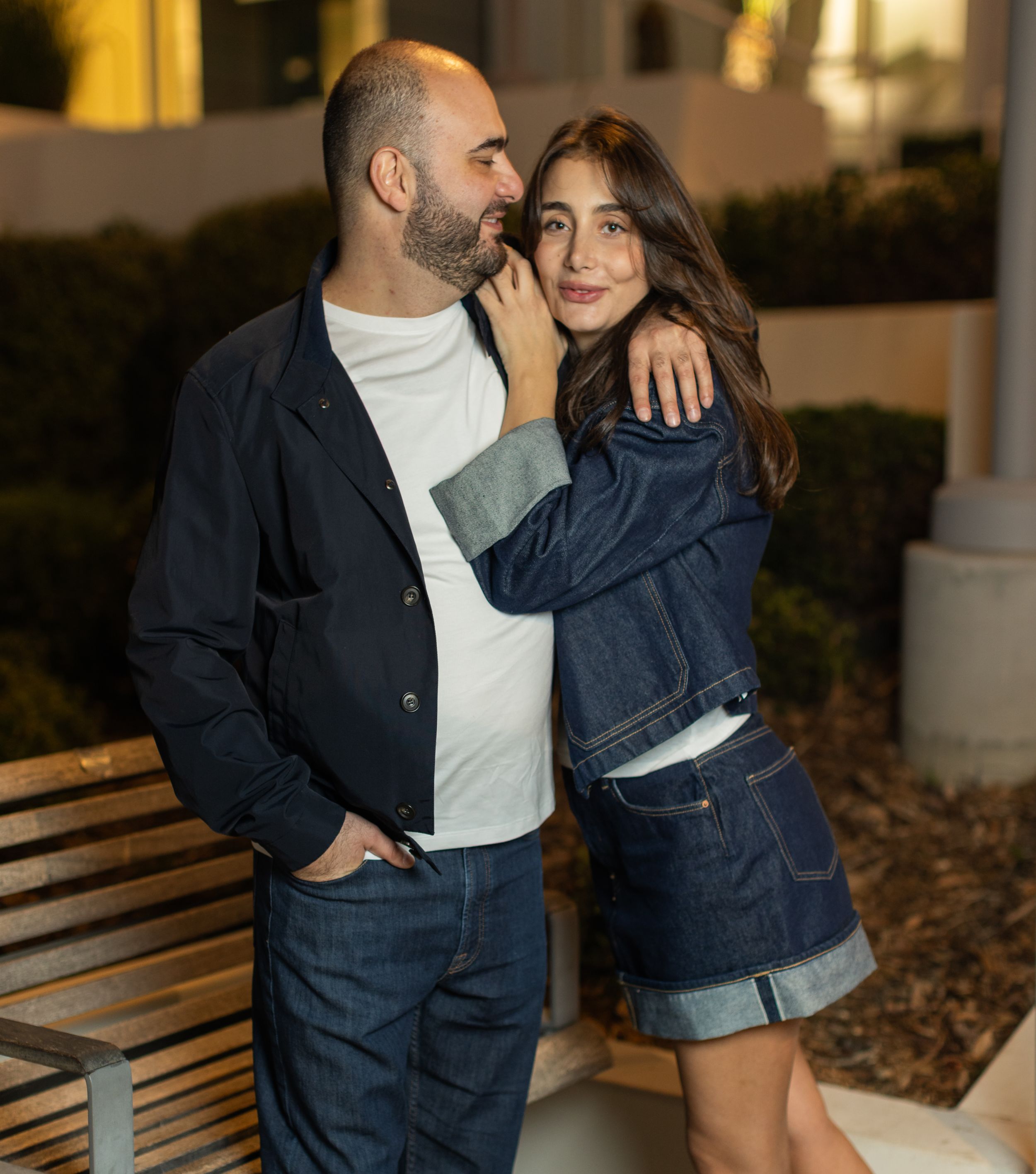 Romantic couple in matching denim outfits posing by wooden bench.