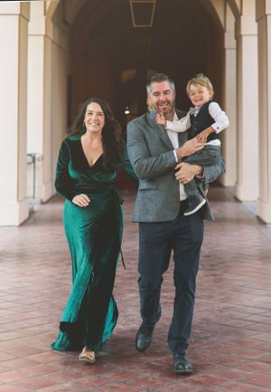 A family walks together through an elegant archway with the woman wearing an emerald green dress.