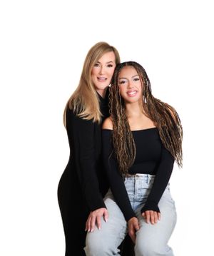 Two women in black tops pose together for a portrait against a white background.