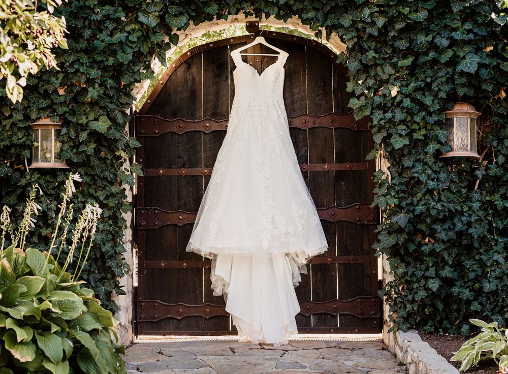 Elegant white lace wedding dress hanging on rustic wooden doors framed by lush green ivy walls.