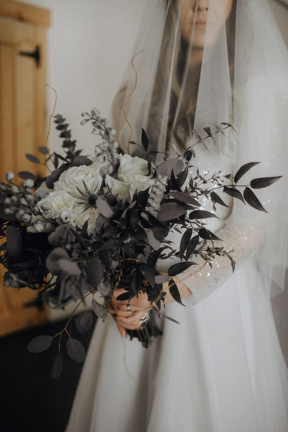 Wedding bouquet with white flowers and black foliage against white dress.