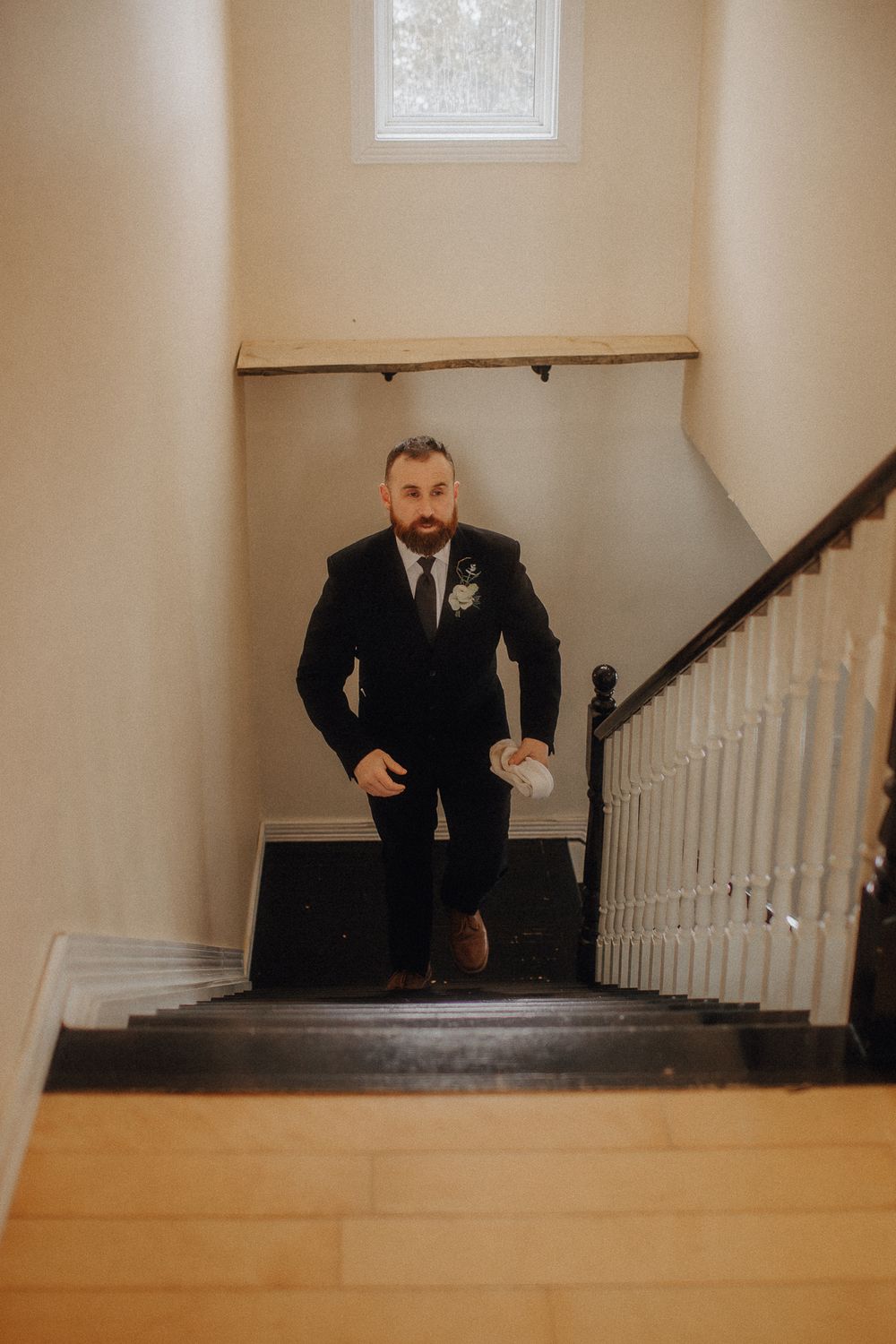 Person in formal suit ascending wooden staircase with white banister.