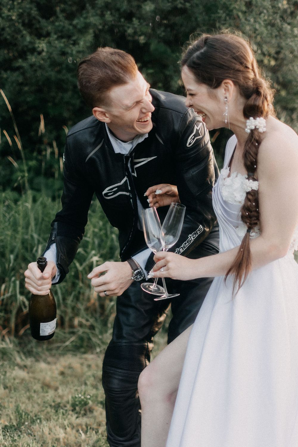 Newlyweds sharing champagne and laughing together during outdoor wedding celebration.