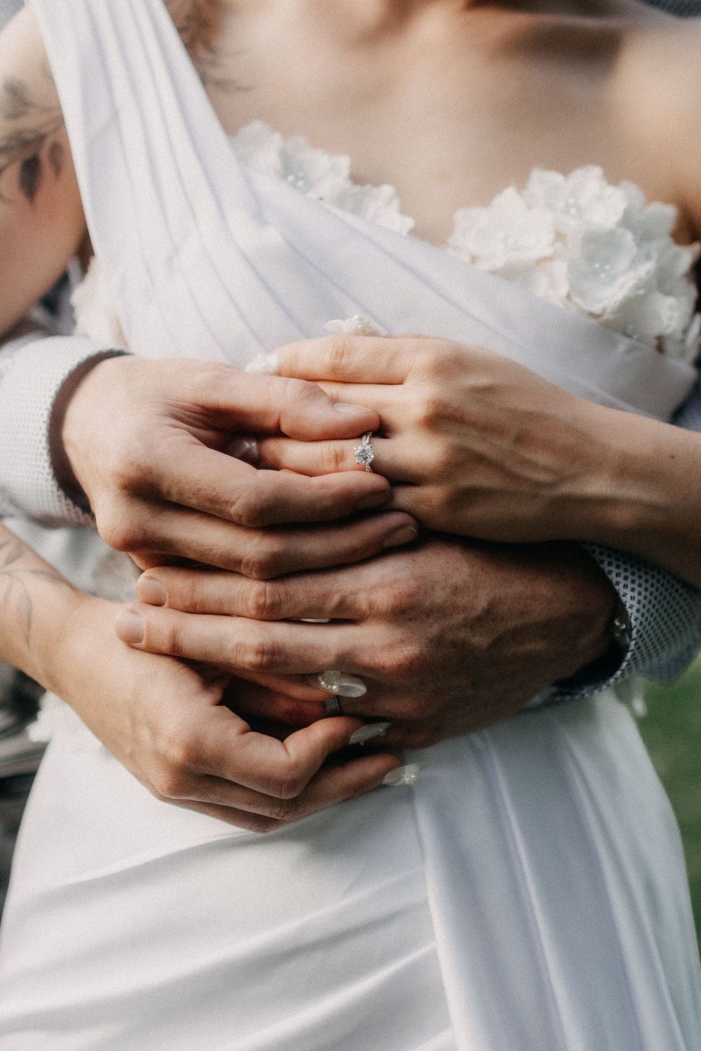 Close-up of hands with wedding rings against white dress fabric.