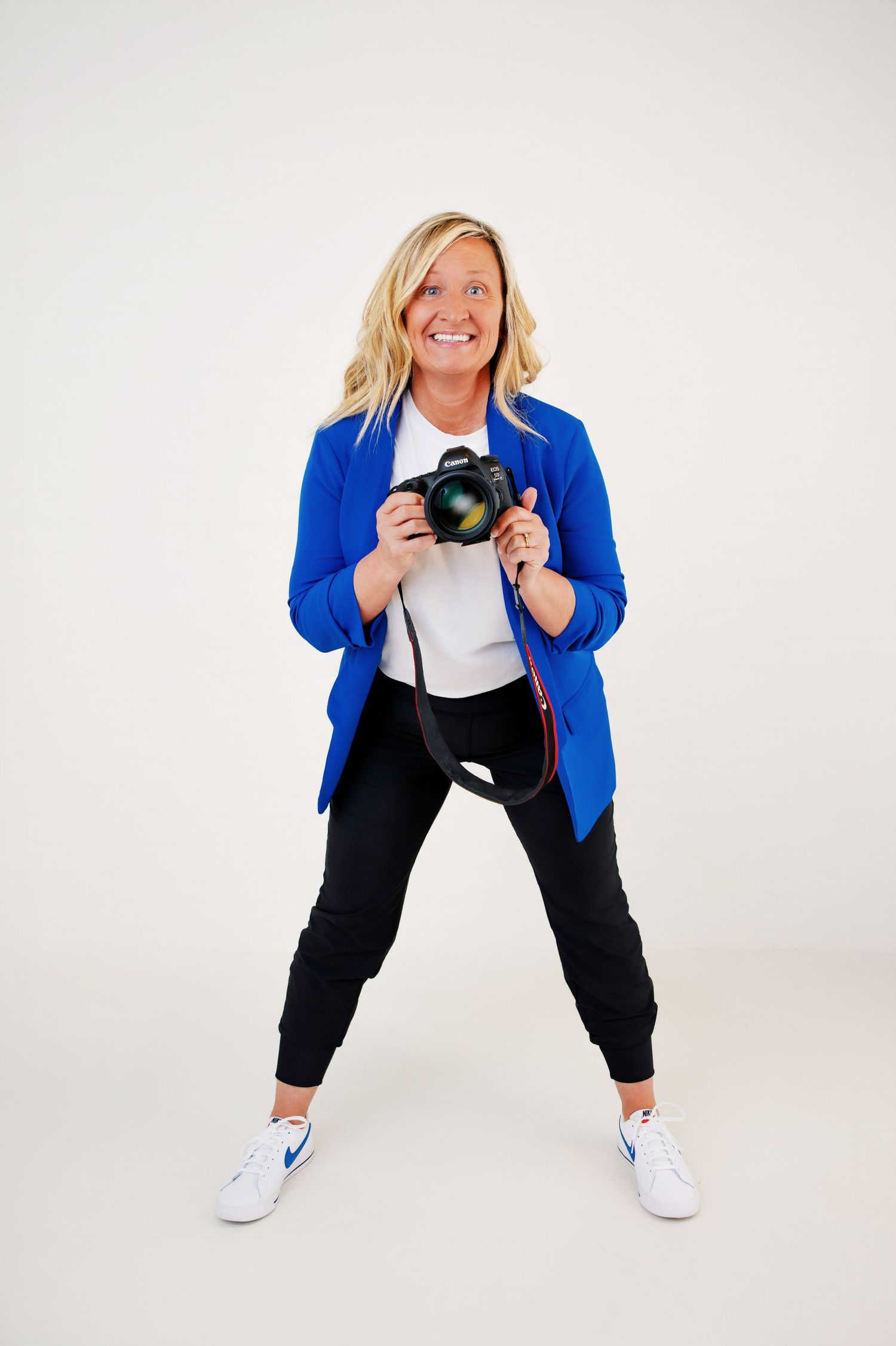 Photo of a Senior photographer holding her camera and smiling very big and leaning forward.