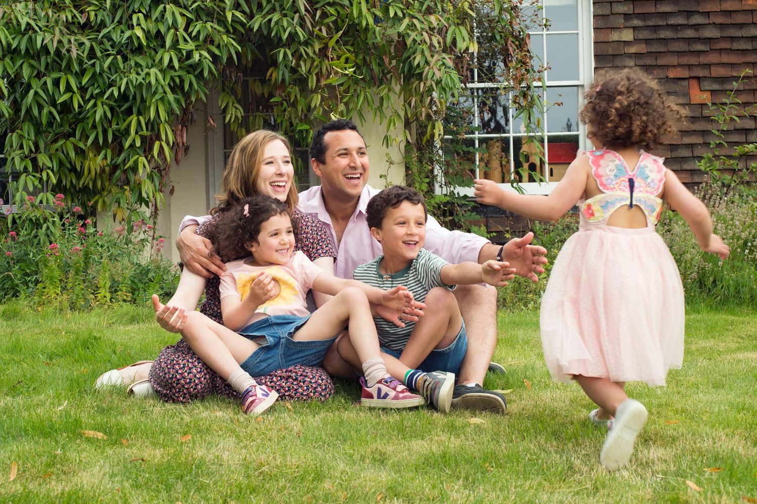 A family sits together on the grass outside their house, smiling for the camera during an outdoor photoshoot in Buckinghamshire