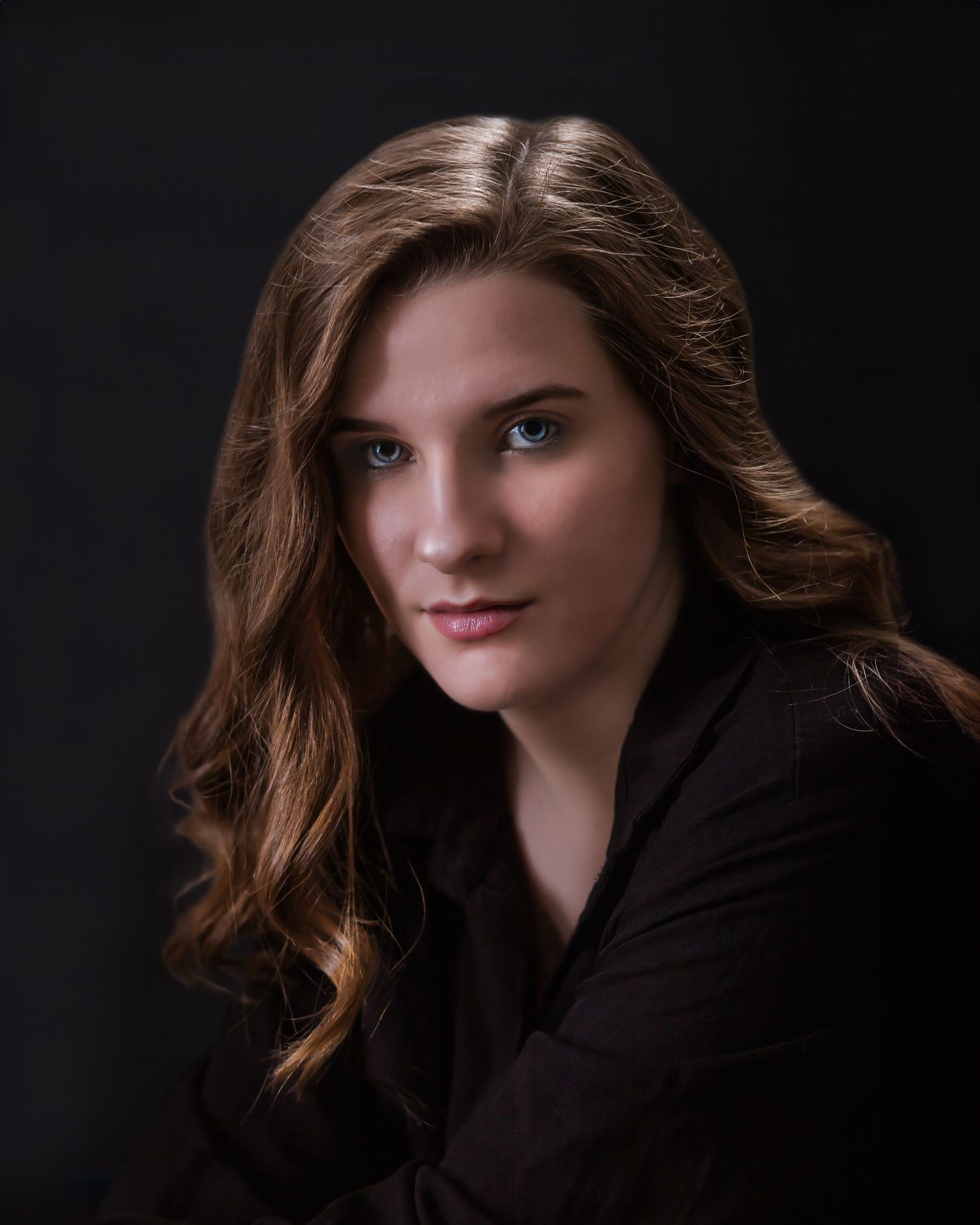 Professional portrait with dark backdrop featuring soft lighting and dark attire.