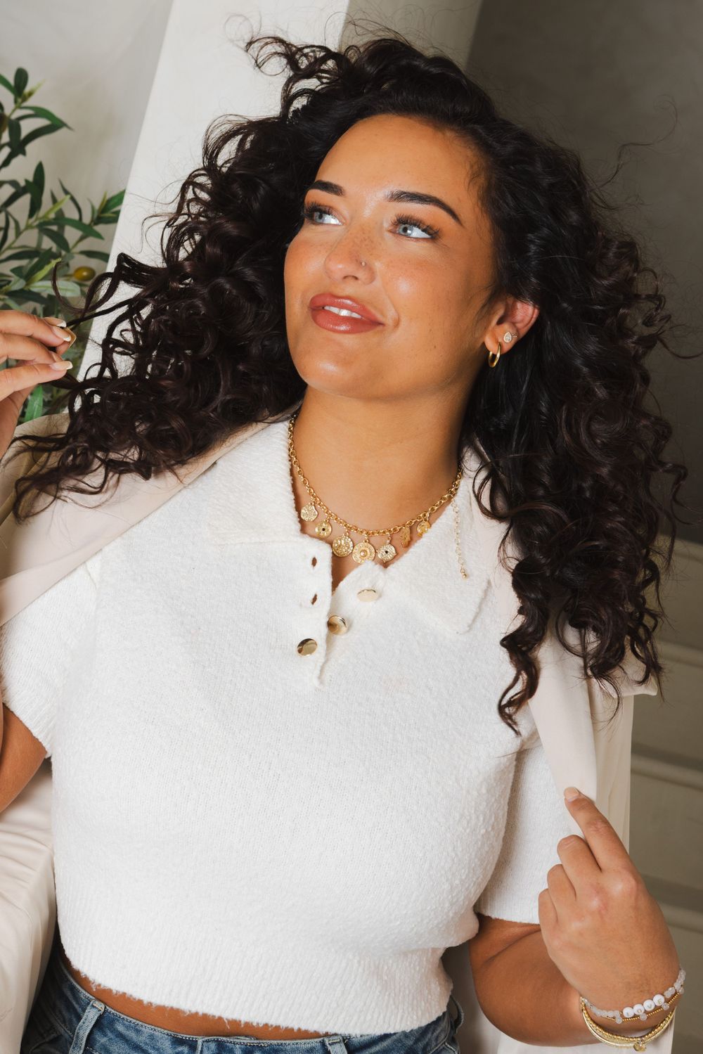 Fashion model in white textured crop top with gold jewelry poses against white background.