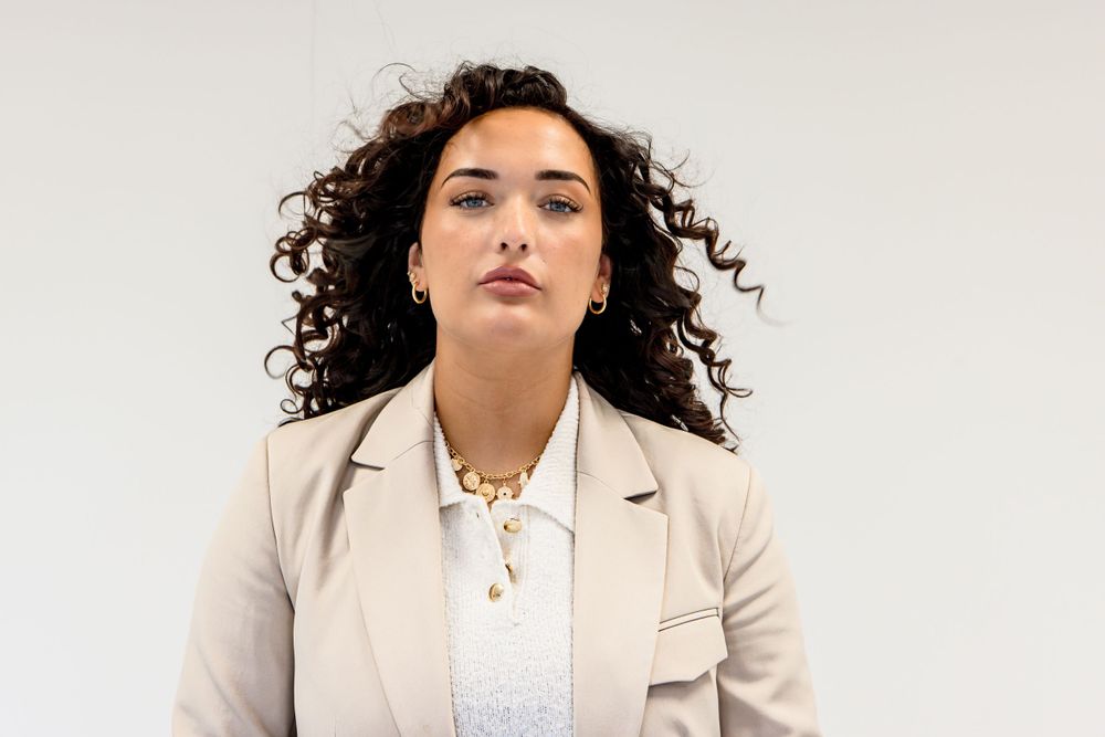Fashion editorial featuring models in beige blazers against minimalist white setting.