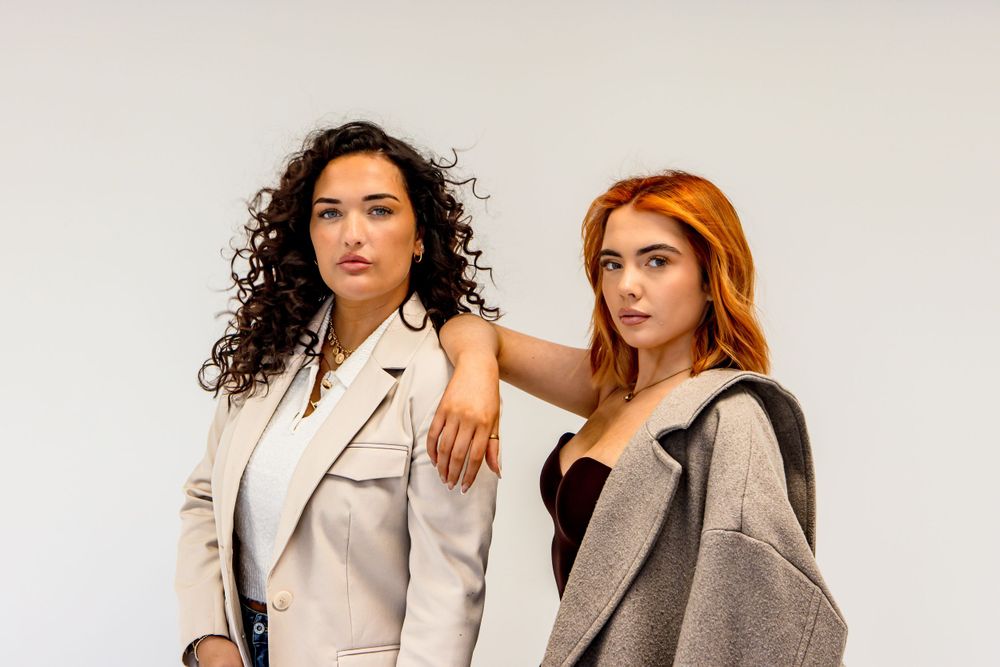 Models pose together wearing coordinated neutral-toned outfits in studio setting.
