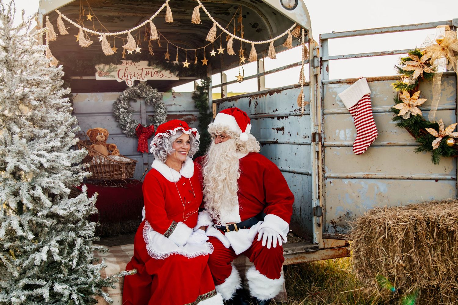 Festive Christmas scene with decorated tree, hay bales, and holiday characters.