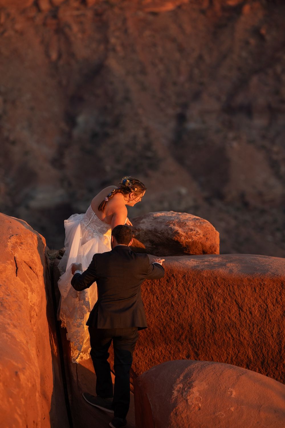 Two silhouetted figures stand on a rocky outcrop at sunset, casting long shadows against the warm orange glow.