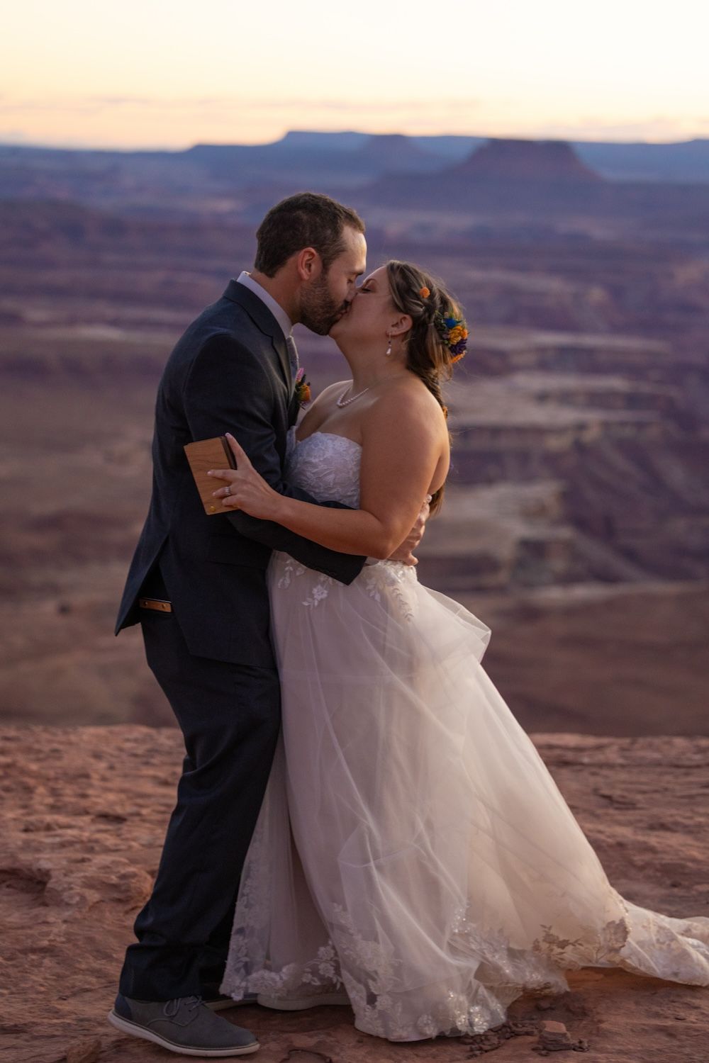 A couple shares a romantic kiss against the stunning backdrop of desert canyons at sunset.