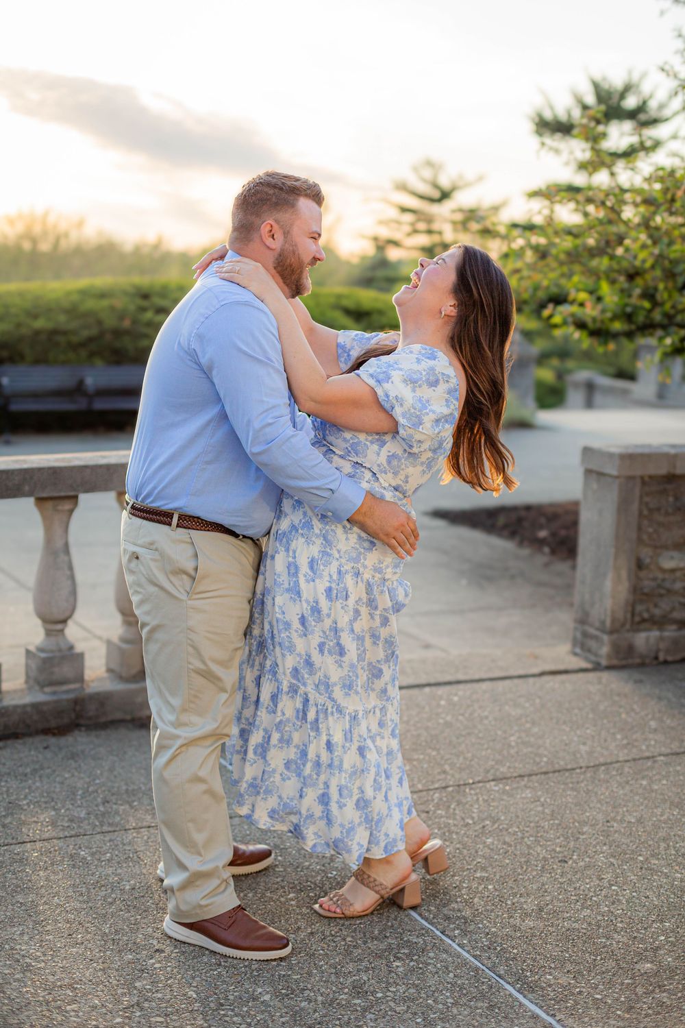 Couple embracing in a romantic moment at sunset on a stone terrace surrounded by landscaping.