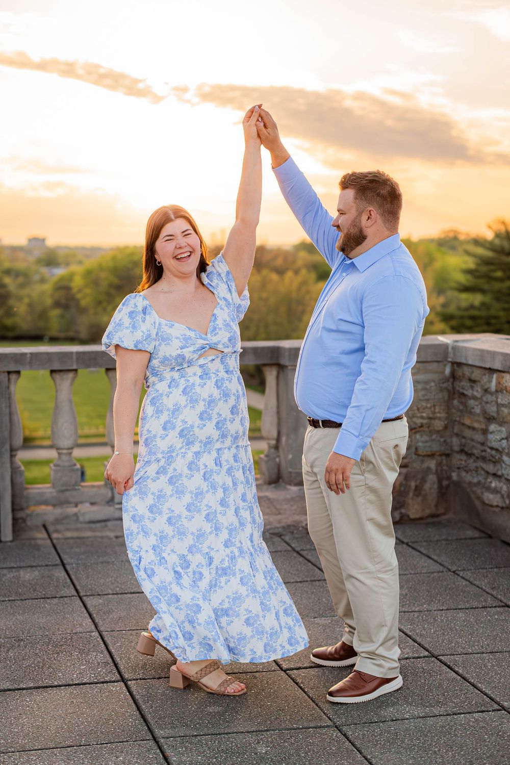 A couple dressed in blue shares a joyful dance moment together on a stone patio during golden hour sunset.