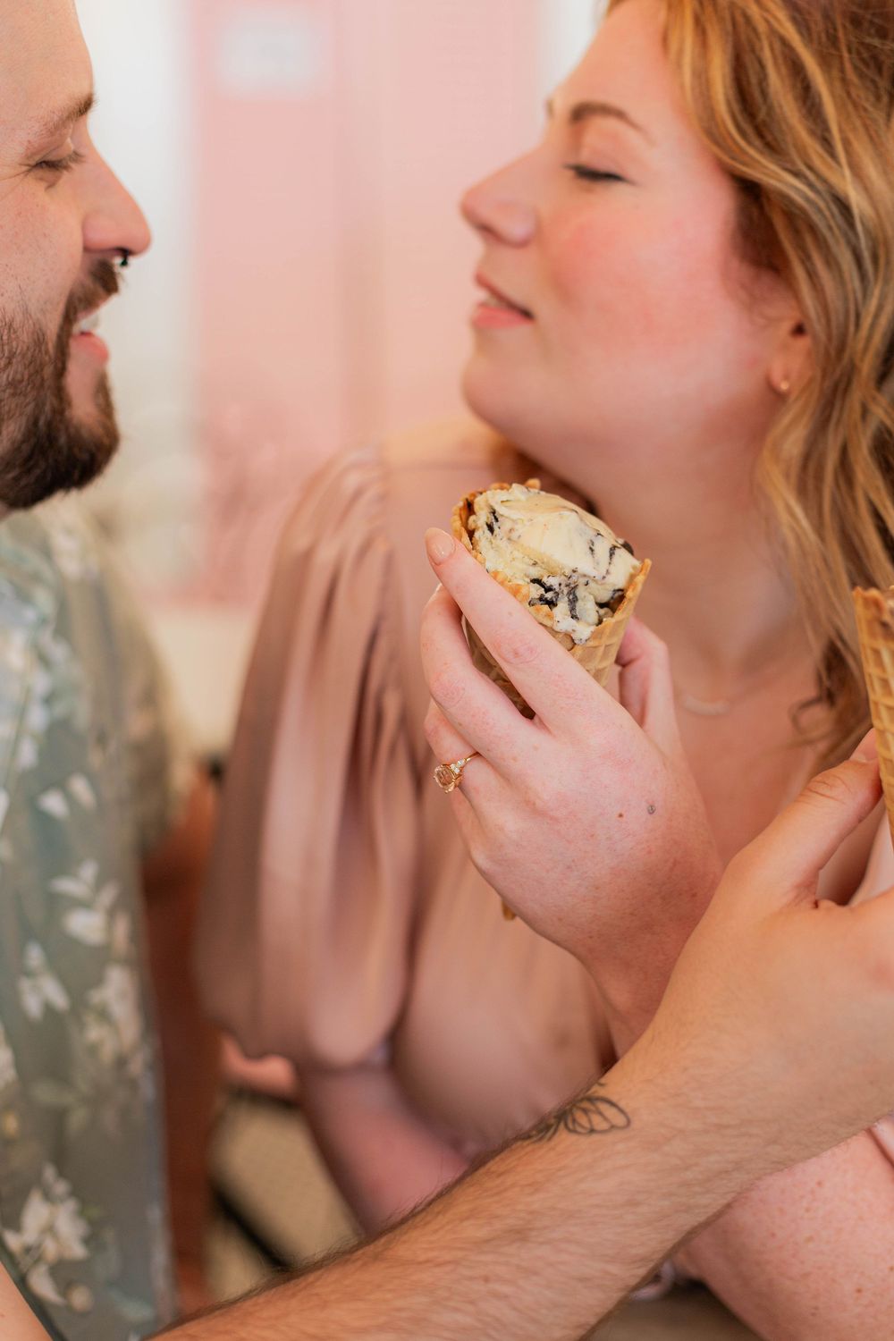 A romantic moment shared between a couple enjoying a sandwich together in soft pink lighting.