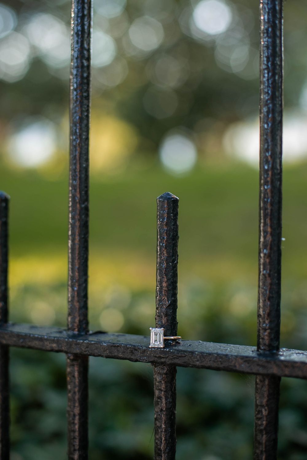 Close-up view of rusty iron fence bars with shallow depth of field and bokeh effect in background.