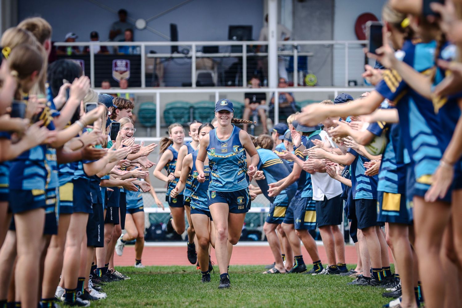 Athletes run through tunnel of high-fiving supporters on athletic track.