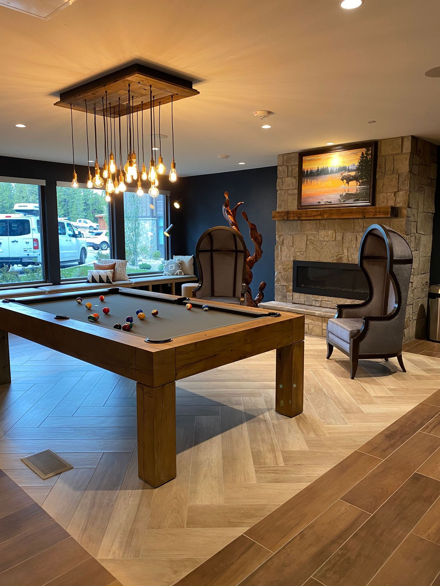 Elegant game room with pool table, designer lighting fixture, and stone fireplace.