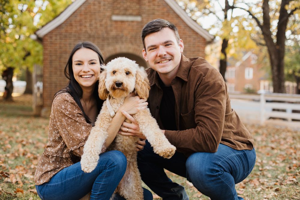 A couple poses with their golden retriever puppy among fallen autumn leaves.