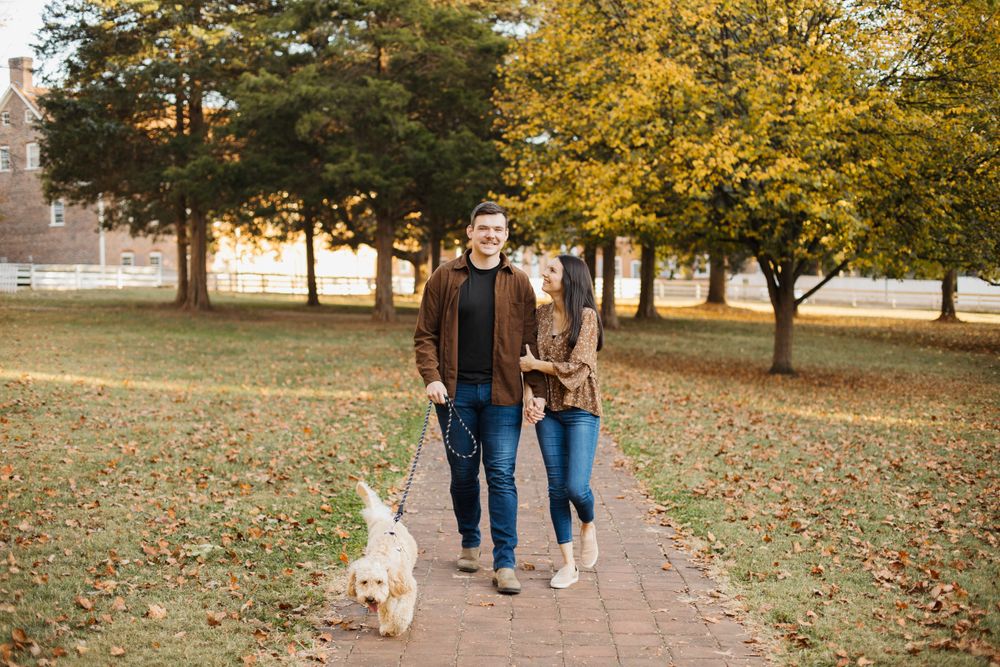 Couple walks with their dog along brick pathway during fall season.